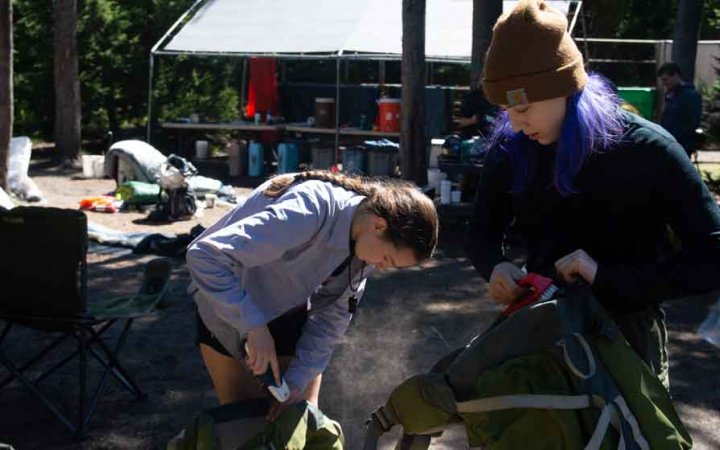 two teens girls packing backpacks in preparation for outward bound backpacking expedition 